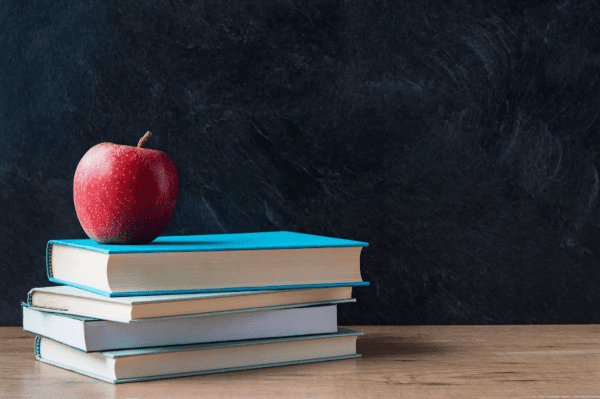 An apple kept on four hard bound books in front of chalk board